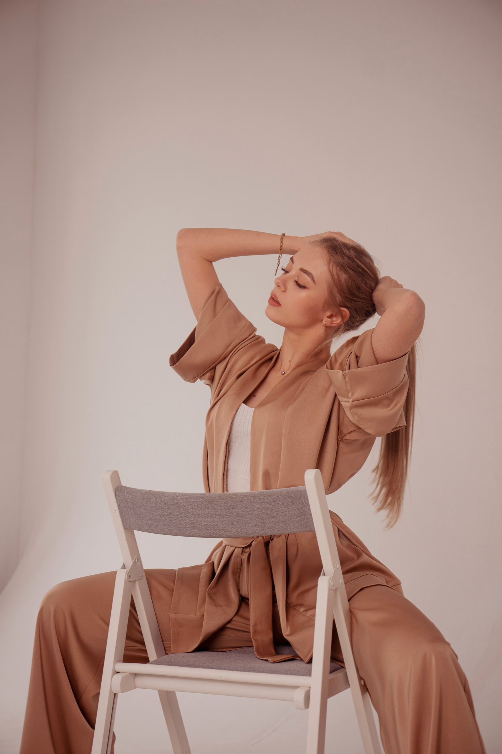 Mulher de conjunto caramelo sentada numa cadeira branca